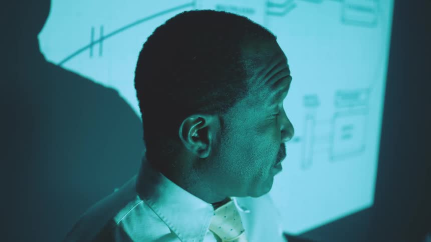Office worker gives a presentation in front of graphics projected on a wall