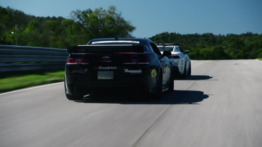 Two cars are driving on a road during the spring