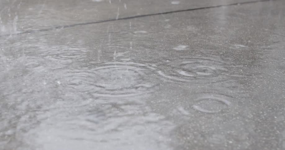 Raindrops fall on a wet sidewalk