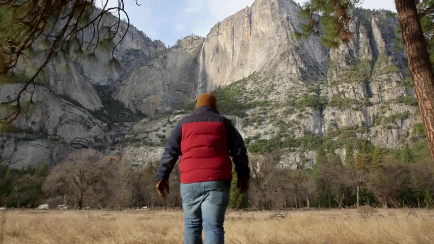 A man is walking over a field towards a mountain