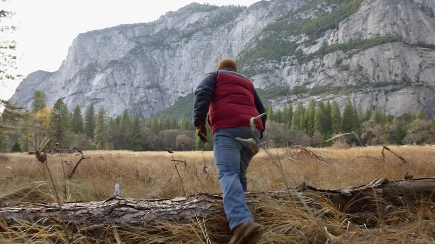 A man steps over a fallen tree as he walks in a field