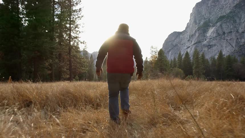 A man in an orange jacket walks across a field