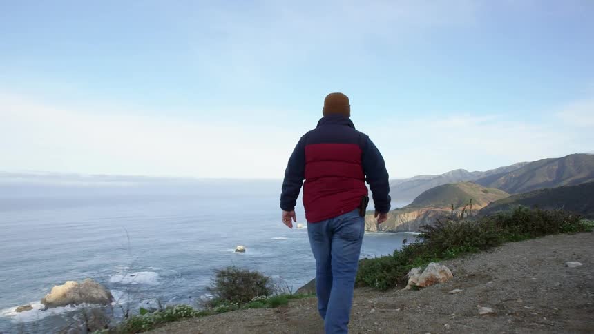 A man walks near the edge of a cliff by the shore