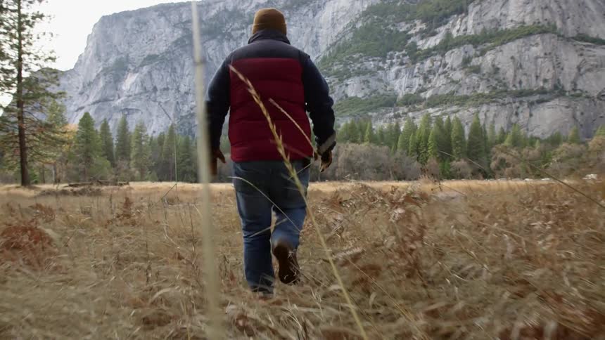 A man is hiking in yellow grass towards a mountain
