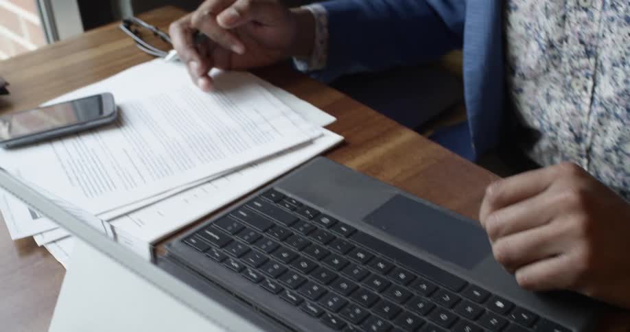 A person working on laptop and checking paperwork