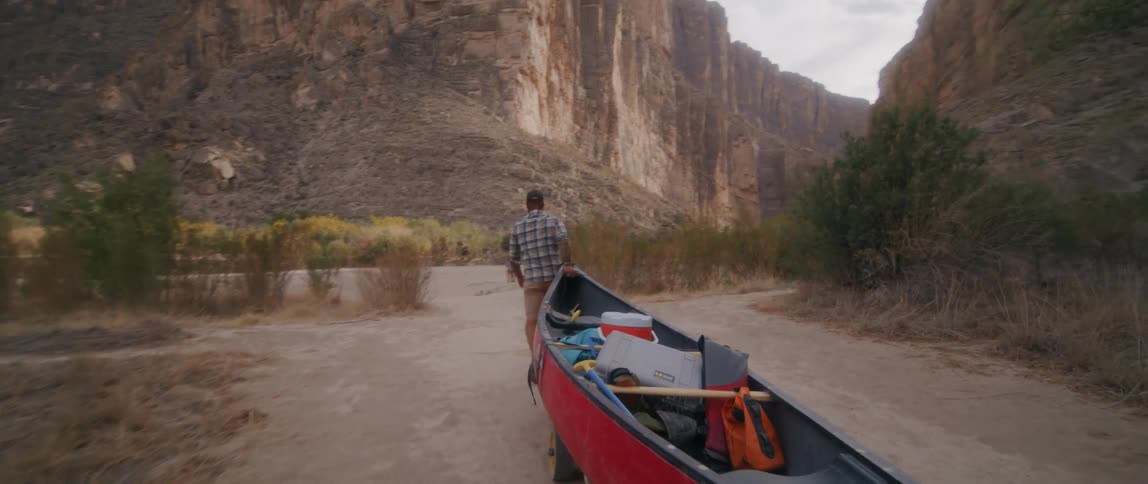 A man pulls a boat on a trailer behind him as he walks toward a group of people in a canyon