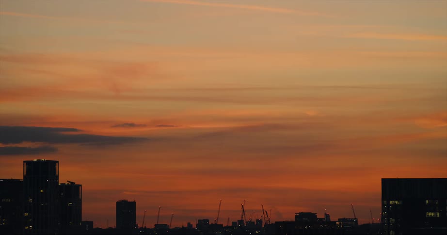 Orange clouds hanging over the silhouette of buildings in the city skyline at sunset