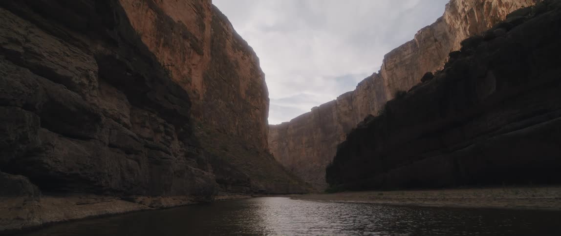 There is a small piece of land along a canyon river as sunlight shines on the ripples in the water