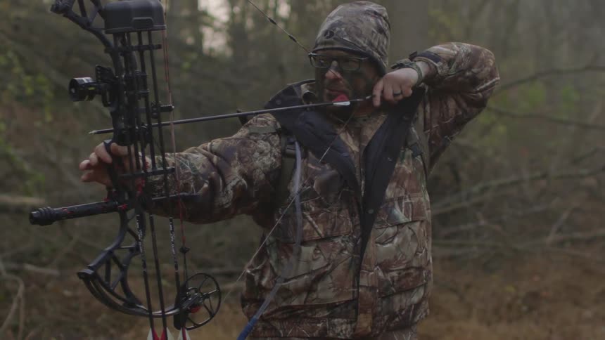A man is aiming a large bow wearing all camouflage