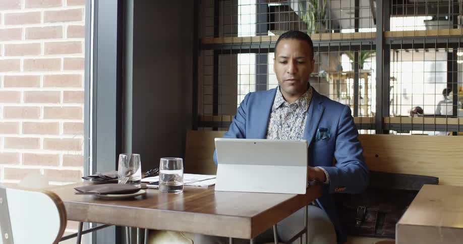 A man is sitting at a table writing and looking at a computer