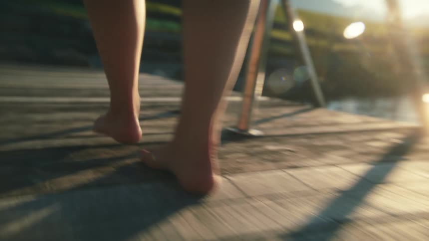 Person walks barefoot across decking passing ladder with mountains in the distance