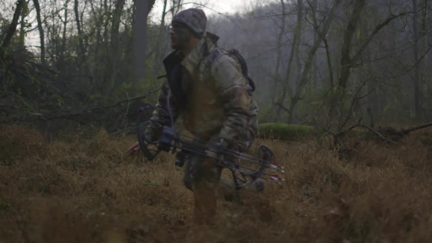 A man carrying a bow sneaks across a field