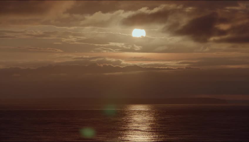 The ocean waves reflect colors from the orange sunrise above