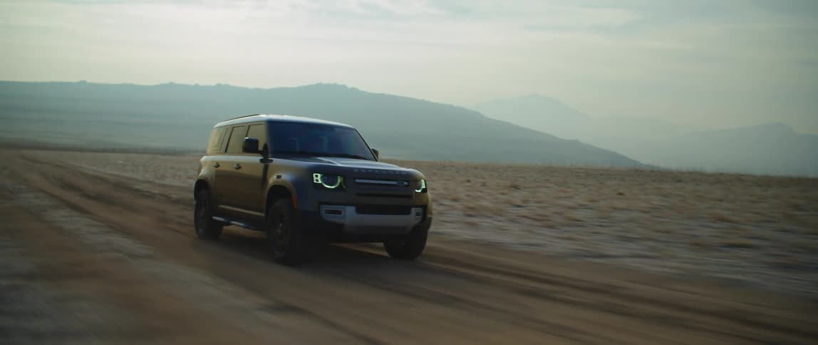 A vehicle travels along a dirt road through an arid countryside during the day