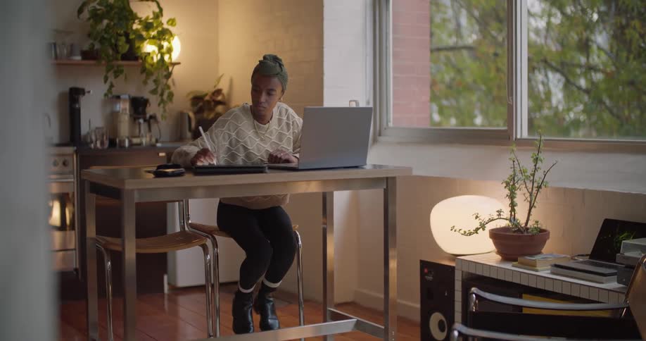 A woman writes as she looks at her laptop