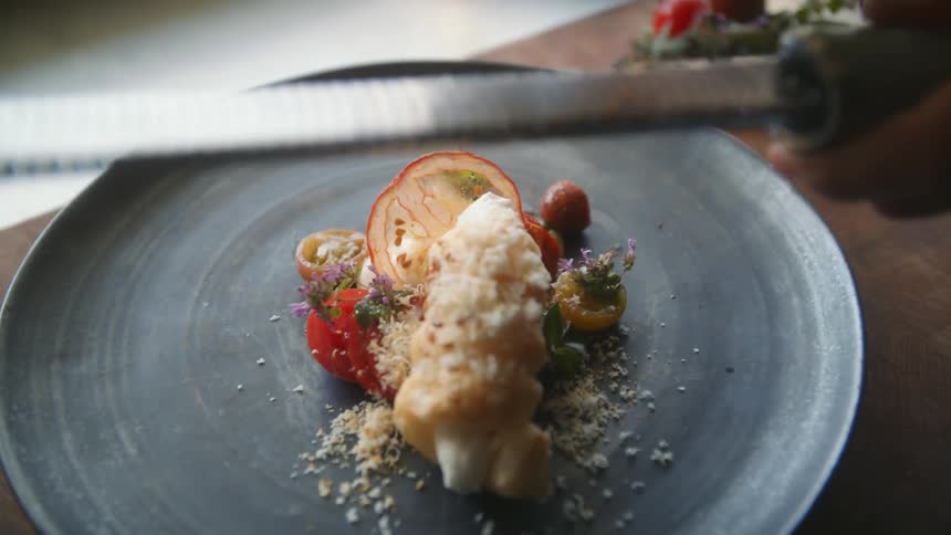 A person grating cheese over a plated entree