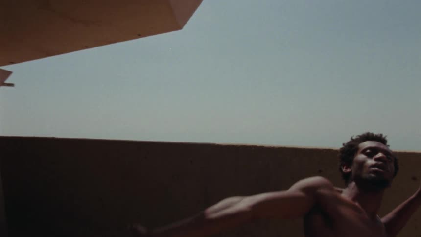 Shirtless professional dancer dancing on a balcony outdoors during a sunny day