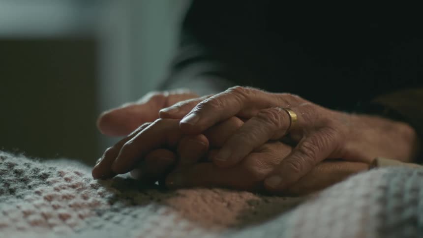 Close up of the hands of an elderly man caressing the hands of a patient laying in bed