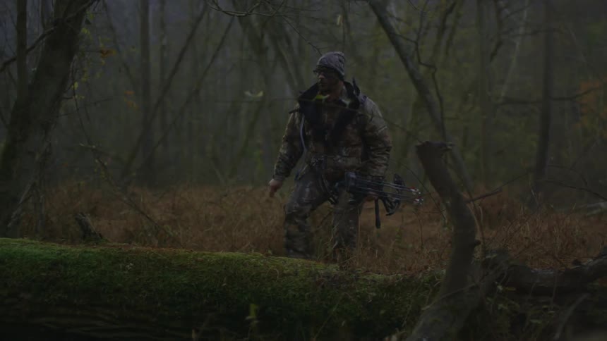 A man wearing camouflage walks in the woods