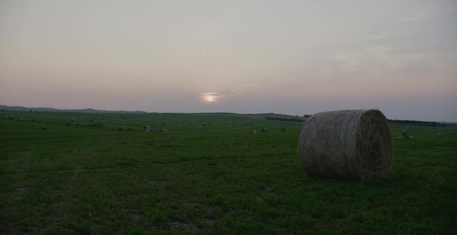 A single hay bale in front of the sun setting over a green field