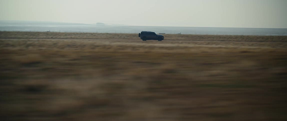 A black truck is traveling fast on a road across the desert