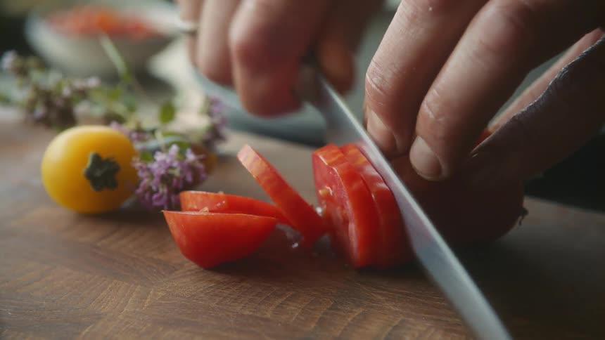 A person uses a knife to cut vegetables on a wooden cutting board