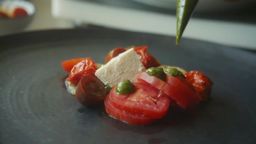 A chef piping sauce onto a plated meal with tomatoes and cheese