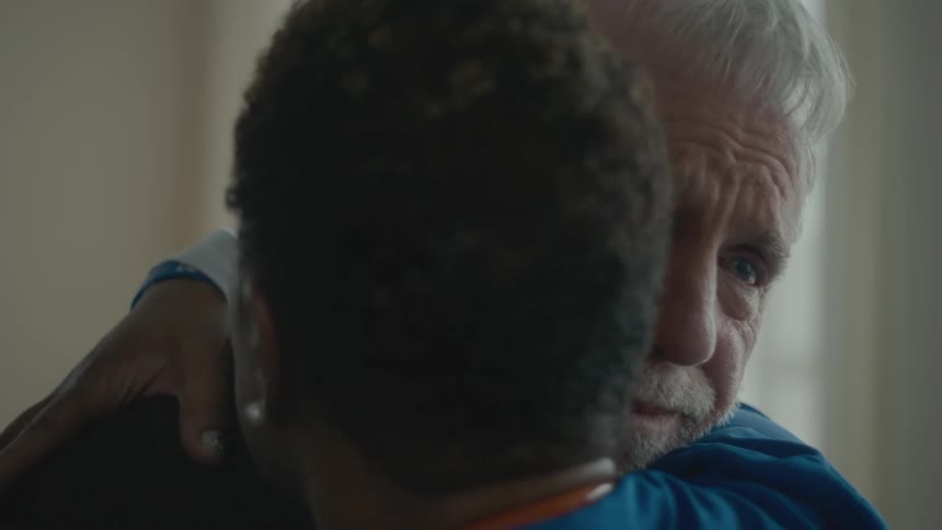 A sad man and a woman embrace while standing indoors