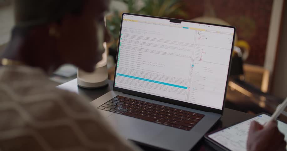 Black woman sitting at the desk inside her house using her laptop and writing code
