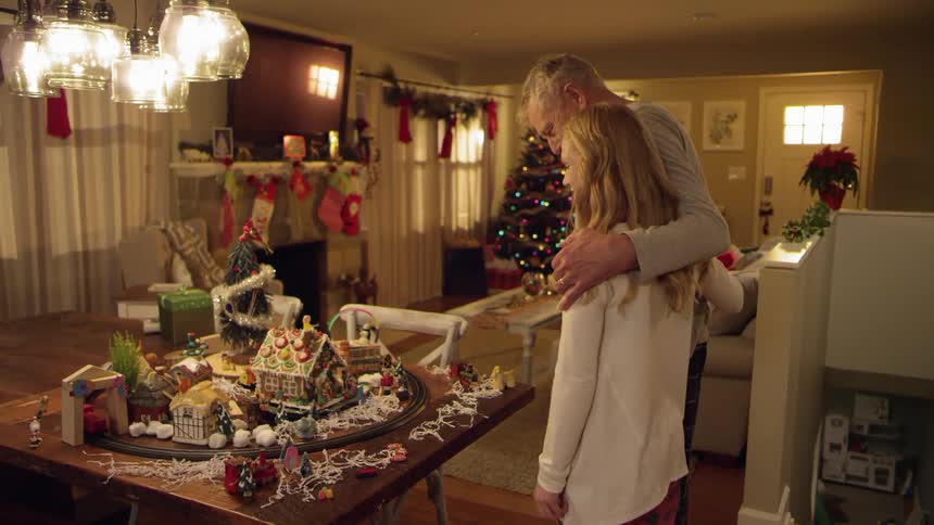 A young woman running up to hug an elderly man who is observing a christmas train set