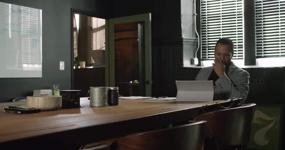 A man is sitting at a large table using a computer and writing