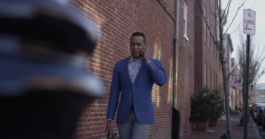 A man holding a bag walks while talking on a phone