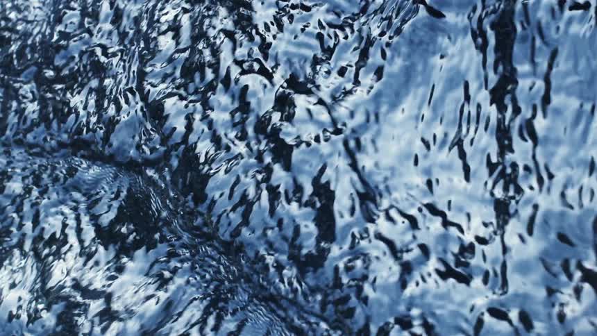 The sky and light reflect on the surface of a flowing swirling river