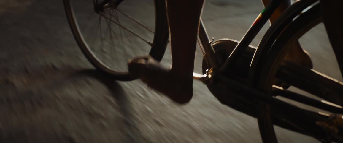 A person with bare feet is riding a bicycle on a sidewalk at night