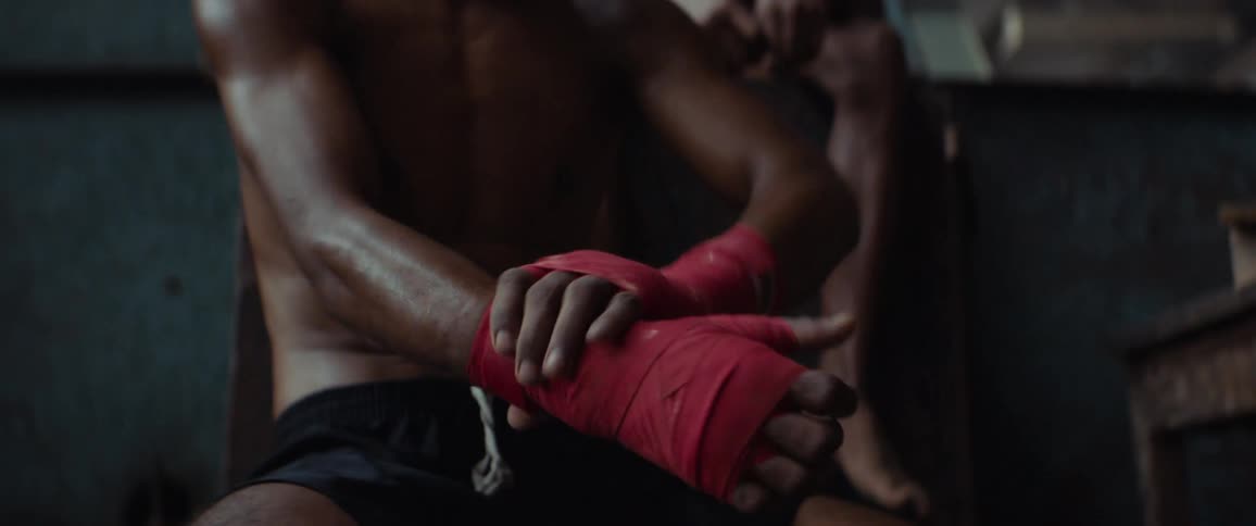 An athletic man with his shirt off puts a wrap on his hand