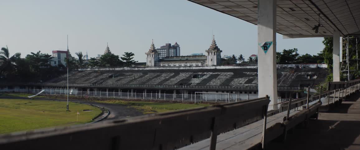 A person exercises by running up the stairs of the stands surrounding an old athletics field during the day
