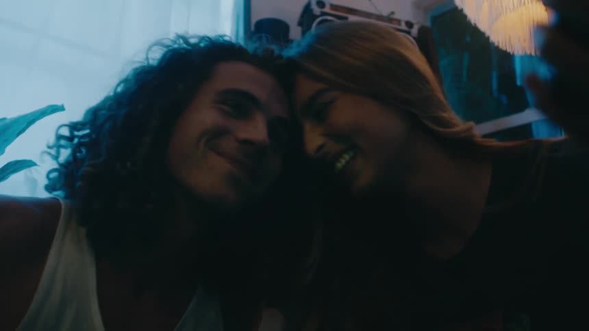 A man and woman take a selfie together while sitting on the floor before sharing a kiss