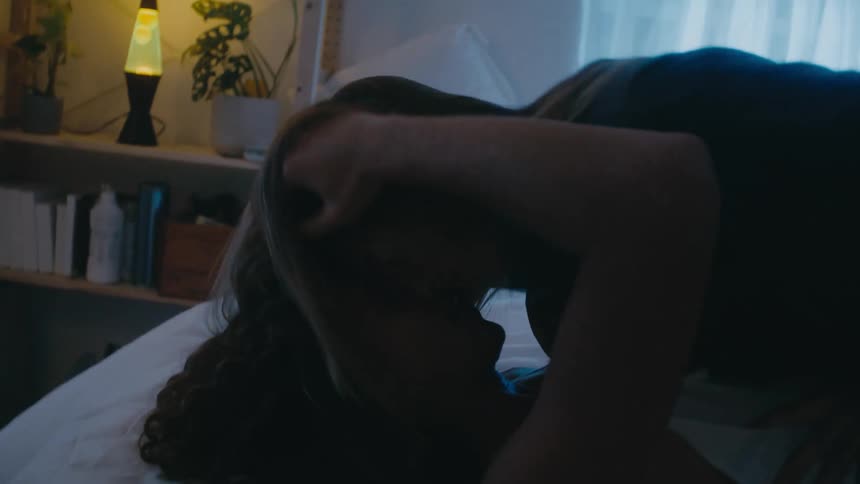 A man and woman are on a bed having a heavy makeout session