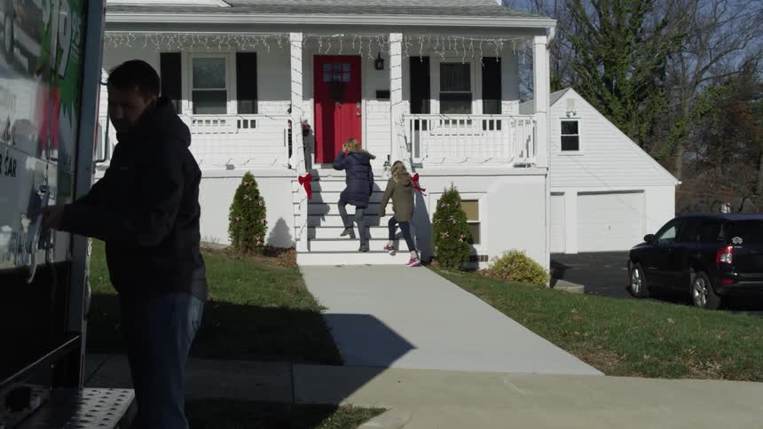 A man lifts the gate of a u-haul while a woman and child enter a home
