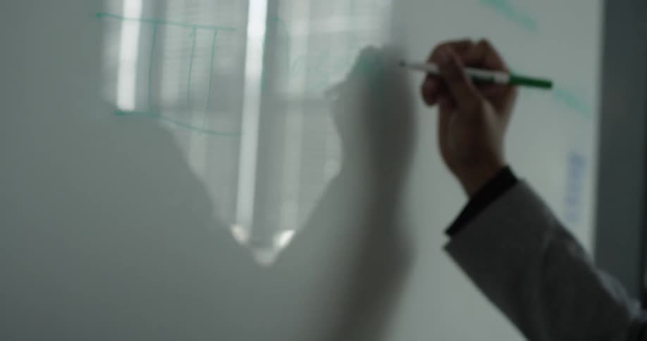 A person is holding a paper while writing on a board