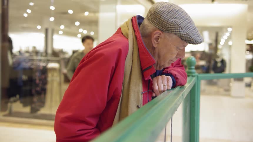 An old man leans on a railing in a mall