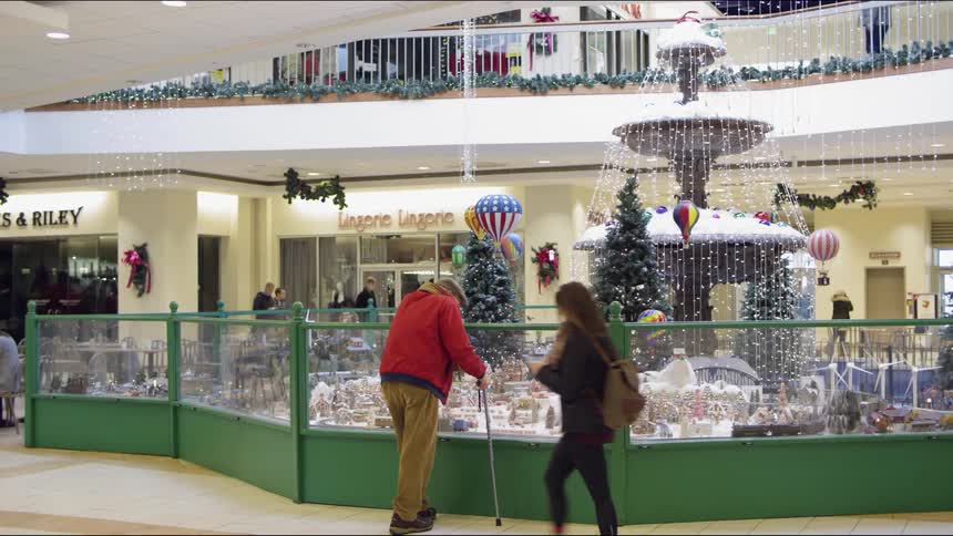 A man is leaning over a display in the mall as people walk around