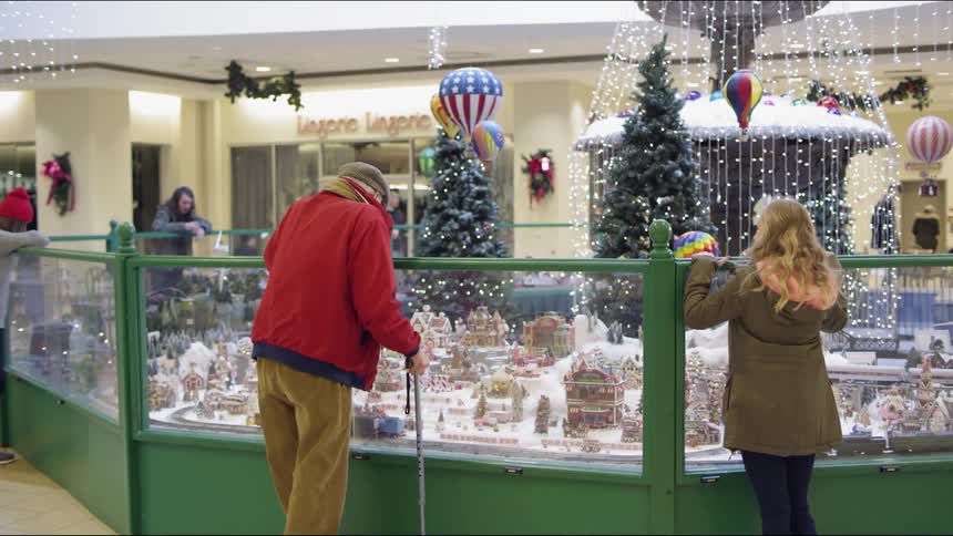 An elderly man observing a model train travelling through a toy village in a christmas display