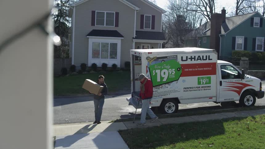 A man unpacks a u-haul as a man with a cane follows