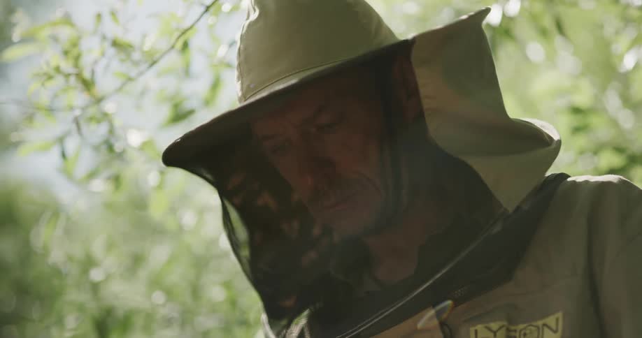 A man is in a beekeepers suit with bees flying all around him