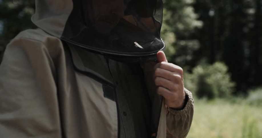 A man is in a field donning a beekeeper suit