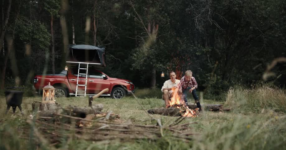 A man and his son are sitting in front of a campfire in the woods