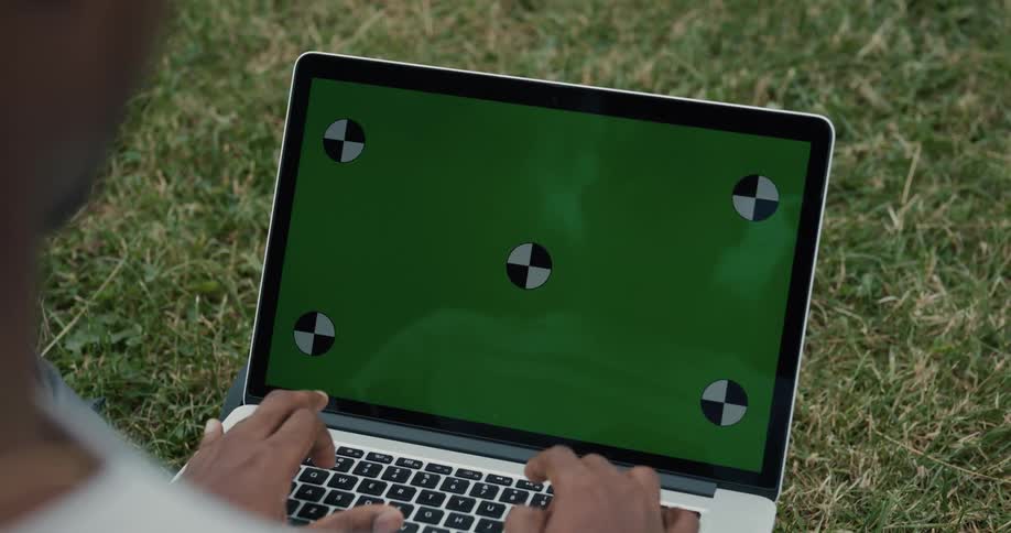 A man is sitting outside on the grass typing on a laptop computer