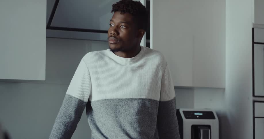 Young black man putting a coffee mug on the coffee machine in the kitchen and waiting for his coffee while using his smartphone