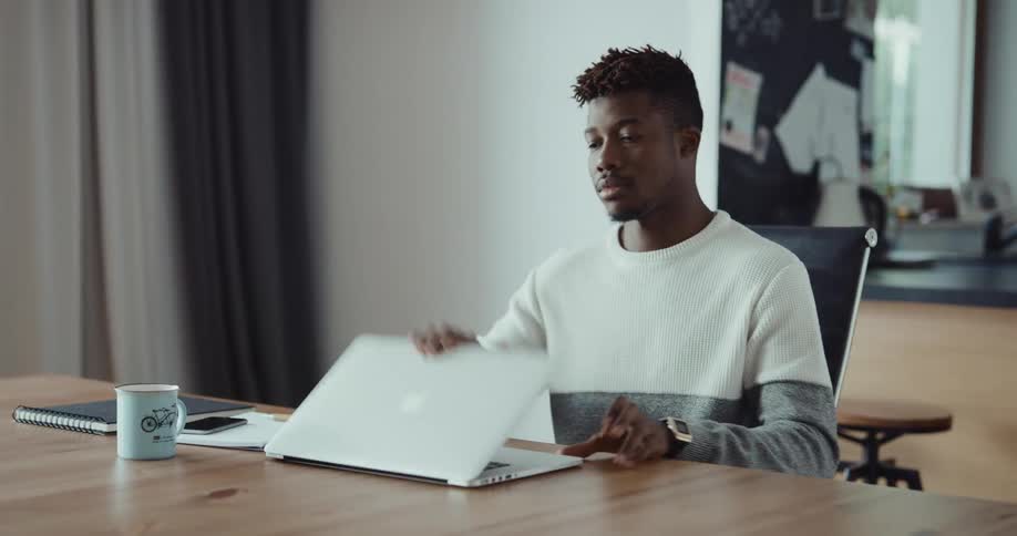 Man typing on laptop rubs his forehead briefly before getting up and leaving